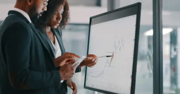 Two professionals collaborating on business data using an interactive digital display.