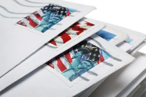 Stack of mailed envelopes with U.S. flag and Statue of Liberty postage stamps.
